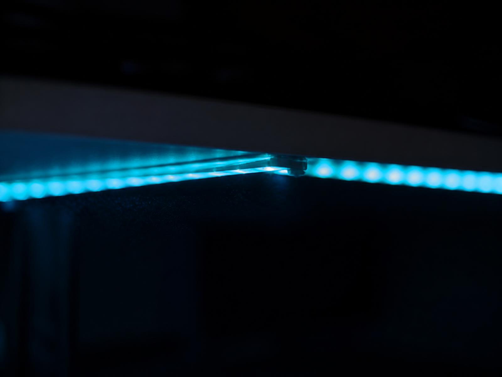 Close-up of a cyan LED strip glowing under the edge of a white desk in a dark room